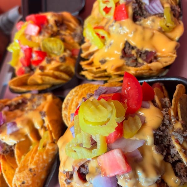 Four servings of nachos with cheese sauce, ground meat, tomatoes, red onions, and pickled peppers.